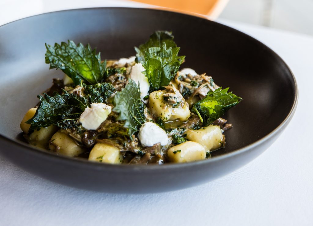 A black bowl filled with potato gnocchi, goat and stinging nettles