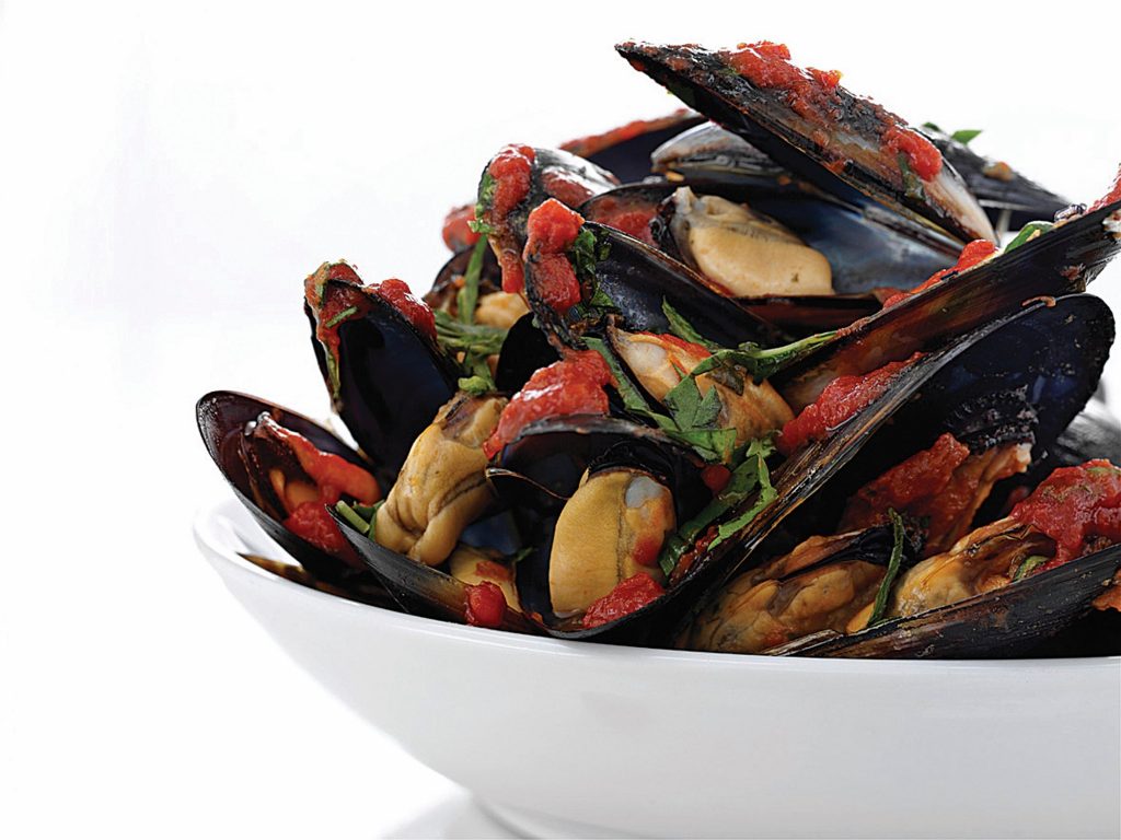 A white bowl of mussels with tomato and chorizo