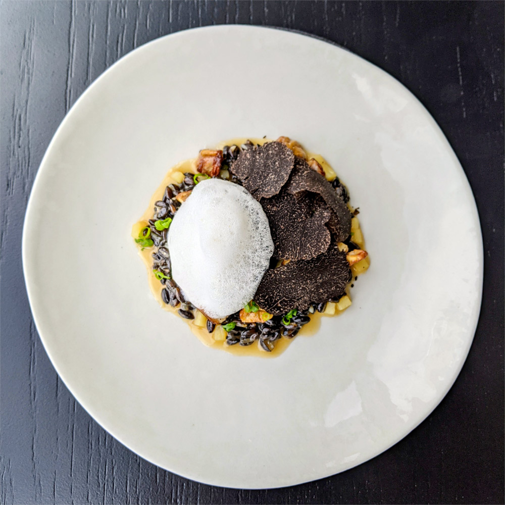 A white dinner plate featuring black barley and potato risotto